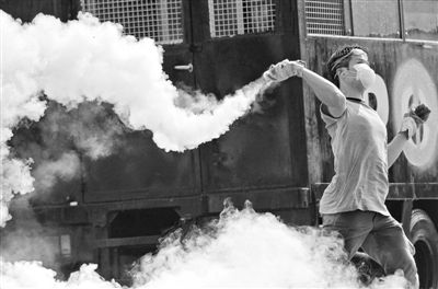 12月2日，泰國曼谷，一名反政府示威者在總理府附近向負責執(zhí)勤的警察投擲催淚彈。英拉請求示威者不要再試圖占領政府工作部門，不要逼迫政府工作人員選邊站。