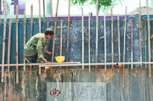 　　烈日下，狹窄的架子上，工人正用錘子固定樁基。