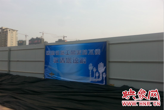 道路南側(cè)圍起了白色的圍擋，墻上標(biāo)示著“因地鐵施工帶來的不便敬請(qǐng)您諒解”的提示牌。