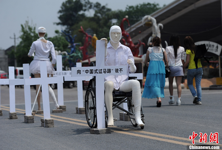 4月16日，重慶市洋人街上擺放著兩個受了傷的塑料人像“模特”，旁邊十字架上寫著向“中國式過馬路”說不