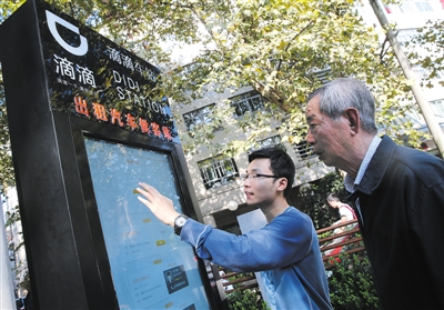 10月15日，滴滴工作人員（左）指導(dǎo)乘客使用“滴滴車(chē)站”的電子屏預(yù)約出租車(chē)。