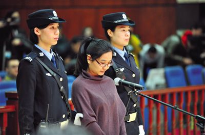 被告人盧梅低著頭，站在朝陽法院刑事審判庭的被告席上。