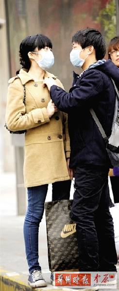 公交站臺上，一對年輕人戴著口罩，系緊衣領(lǐng)。